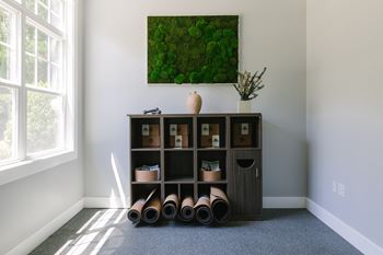 A room with a large window, a shelf with vases and a painting of greenery on the wall.